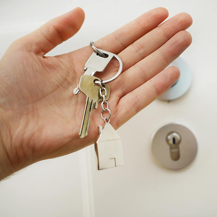 Eine weibliche Hand mit einem Hausschlüssel vor einer versperrten Haustür